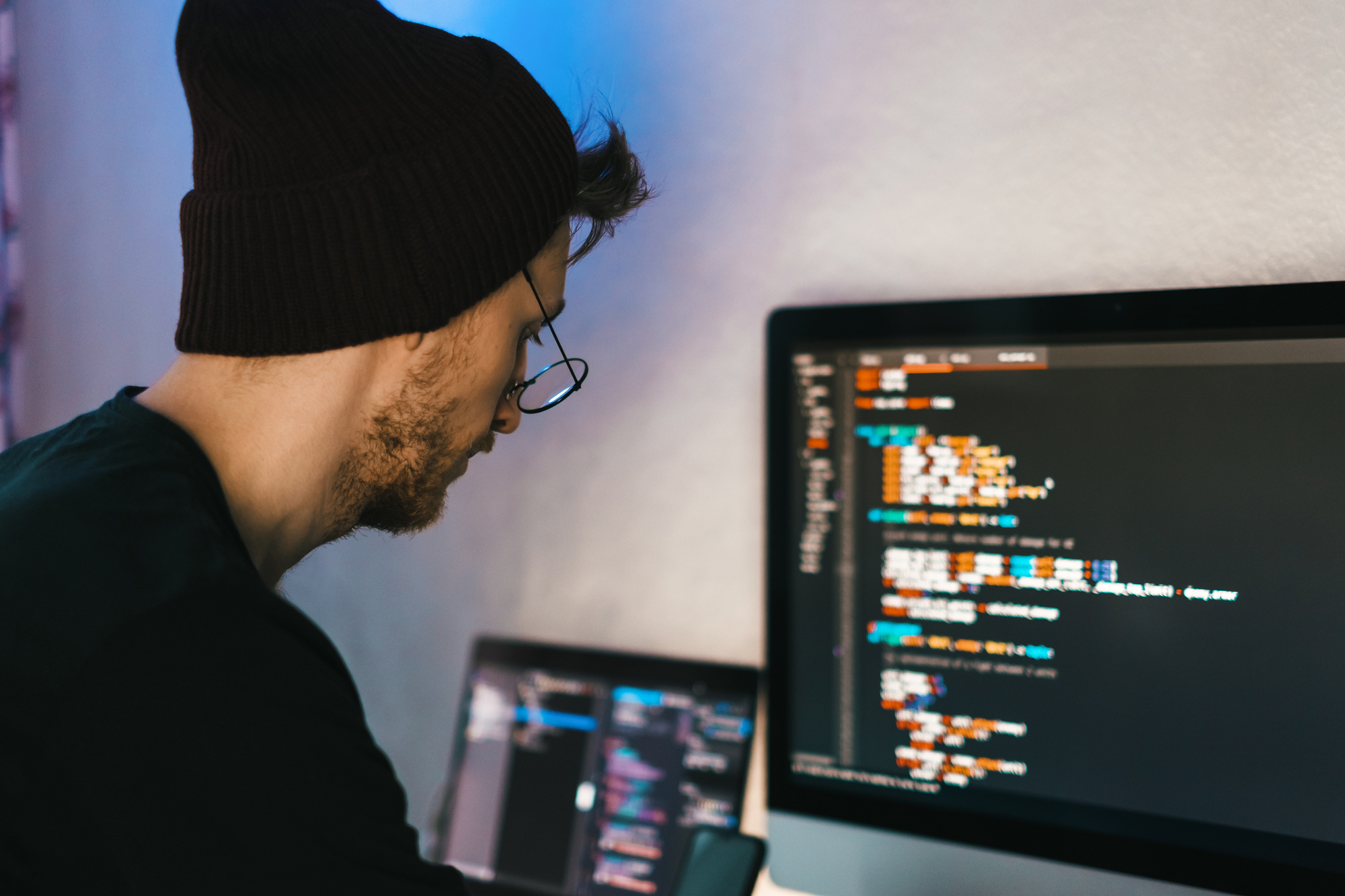 A man wearing a beanie is looking at code on a computer screen, possibly exploring ways to make money off Steam as a games developer.