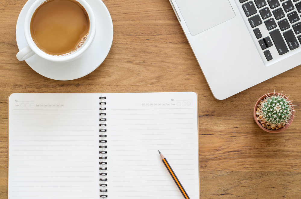 Flat lay of a coffee cup, notebook and a laptop with matched betting tips on a rustic wooden table.